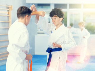 Determined motivated teenagers in kimonos working on hand strikes and martial arts skills in pairs during group training with male instructor ..