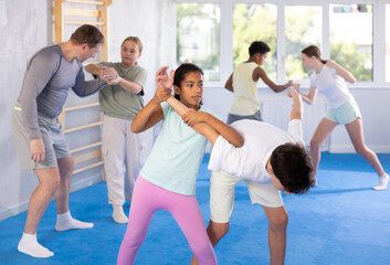 Girls and boys practicing in pair self-defence movements with male trainer supervision
