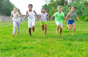Barefoot kids running on green grass on field in summertime.