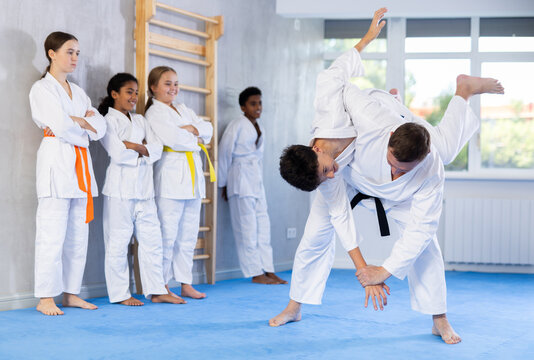 Judo coach shows fighting techniques in sparring with a boy for a group of young athletes - Powered by Adobe