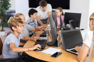 Minor female and male students sitting at computer together with other attendees of IT courses