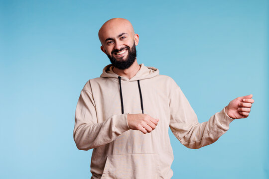 Cheerful arab man promoting product and holding invisible banner for ads portrait. Smiling person pretending to carry placard in two hands and looking at camera with happy expression - Powered by Adobe