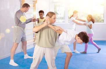 Tweens attending self-defense classes under careful supervision of instructor at training center. Focused girl applying armlock technique in sparring with boy