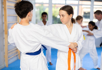 Determined motivated teenage girl working on martial arts skills in pair with boy during group training ..