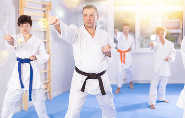 Karate kids in kimono performing kata moves with their teacher in foreground in sports gym during...