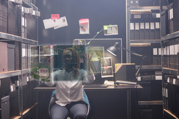 Woman detective looking at evidence in hologram, examining augmented reality image to solve crime in police archive room. Private investigator working with artificial intelligence.