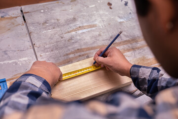 Fototapeta na wymiar Carpenter's hands measuring using a yellow measure tape, closeup view