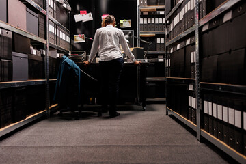 Police detective standing near desk and analyzing clues board in dark office late. African american...