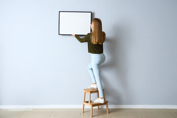 Young woman hanging blank frame on light wall at home - Powered by Adobe