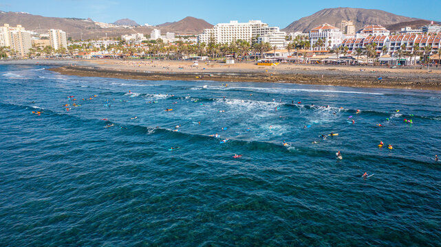 Aerial photo from drone to de surfers in the ocean beachs Adeje Playa de las Americas, Playa Honda In the background Tenerife at sunset. Tenerife, Canary islands, Spain