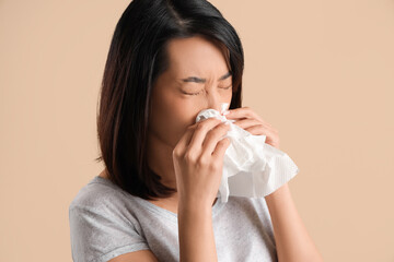 Ill Asian woman with tissues on beige background, closeup