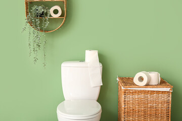 Toilet bowl and wicker laundry basket with paper rolls near color wall