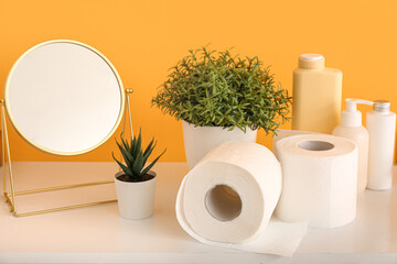 Toilet paper rolls, cosmetic products, plants and mirror on table near color wall