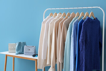 Rack with stylish clothes and bags near color wall