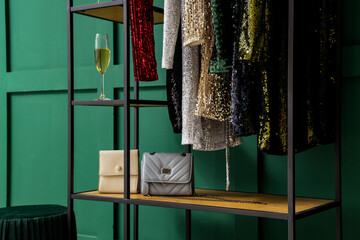 Rack with stylish female dresses, bags and glass of champagne near color wall in boutique, closeup
