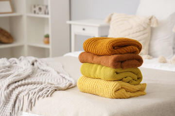 Stack of warm knitted sweaters on bed in bedroom, closeup