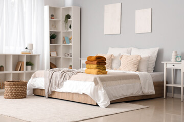 Stack of warm knitted sweaters on bed in modern bedroom - obrazy, fototapety, plakaty