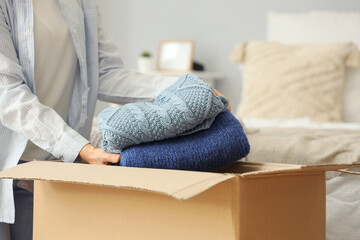 Young woman packing clothes into cardboard box in bedroom, closeup