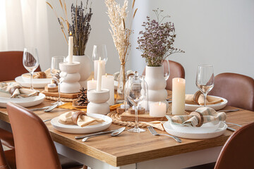 Elegant table setting with dried flowers, burning candles and pine cones