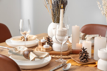 Elegant table setting with dried flowers, burning candles and pine cones