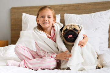 Little girl and cute pug dog with towels in bedroom