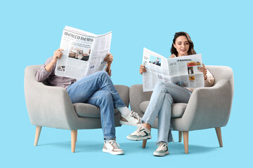 Young couple reading newspapers in armchairs on blue background - obrazy, fototapety, plakaty