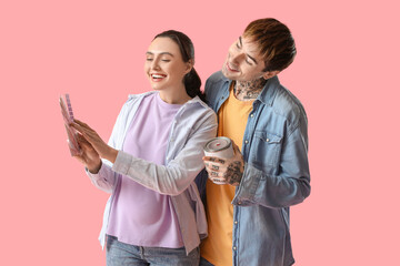 Young pregnant couple with paint can and color palettes on pink background