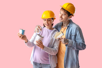 Young pregnant couple with paint cans and brushes on pink background