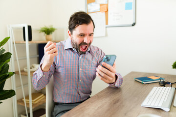 Exxited caucasian boss celebrating good news at work using his phone