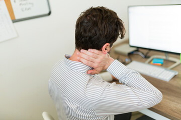 Rear view of a man working at the office with neck pain