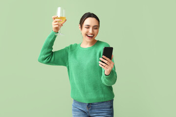 Beautiful young woman with mobile phone and glass of white wine on green background