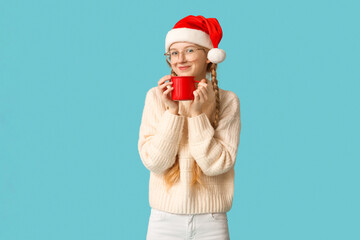 Beautiful young happy woman in Santa hat with cup of tea on blue background