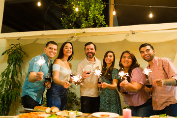 Latin women and men drinking wine after dinner with friends using sparklers