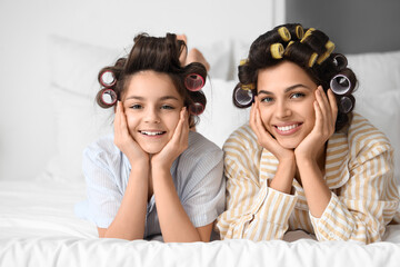 Little girl and her mother with hair curlers lying in bedroom - Powered by Adobe
