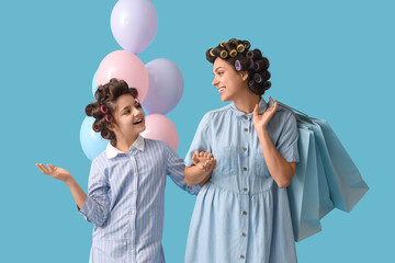 Little girl and her mother with hair curlers holding shopping bags on blue background