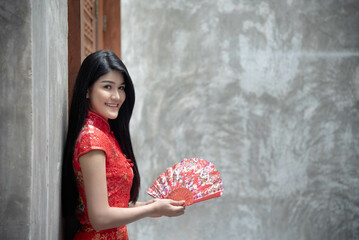 Portrait images of pretty women in asia Wearing a red cheongsam Holding a wooden fan in his hand...