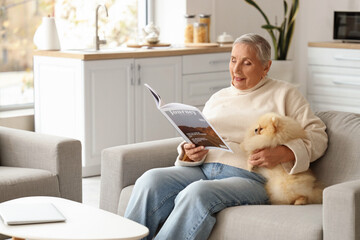 Senior woman with Pomeranian dog reading magazine at home