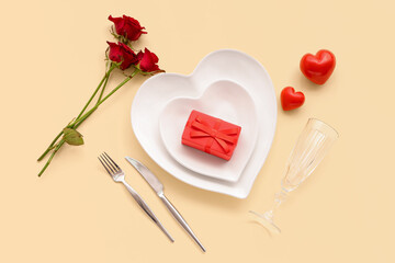 Beautiful table setting with red roses, gift box and hearts on yellow background. Valentine's Day celebration