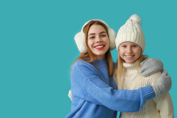 Happy little girl and her mother in winter clothes on blue background