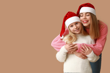 Cute little girl and her mother in Santa hats on brown background