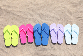 Fototapeta na wymiar Many stylish colorful flip flops on sand outdoors, flat lay