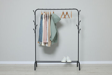 Rack with stylish clothes on wooden hangers and shoes near light grey wall