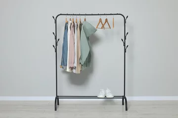 Fotobehang Rack with stylish clothes on wooden hangers and shoes near light grey wall © New Africa