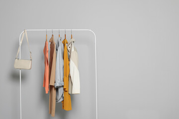 Rack with stylish women's clothes on wooden hangers and bag against light grey background, space for text