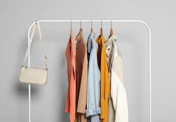 Rack with stylish women's clothes on wooden hangers and bag against light grey background