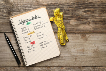 List with products of low, moderate and high glycemic index in notebook, marker and measuring tape on wooden table, flat lay. Space for text
