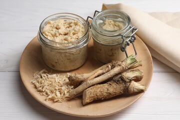Platter with tasty prepared horseradish and roots on white wooden table