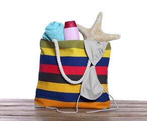 Stylish bag with starfish and other beach accessories on wooden table against white background