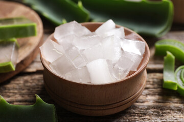 Aloe vera gel and slices of plant on wooden table, closeup