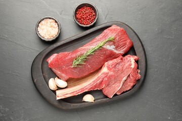Pieces of raw beef meat and spices on grey textured table, flat lay
